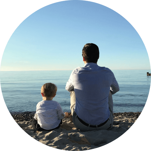 Vater und Sohn sitzen am Stand und schauen aufs Meer
